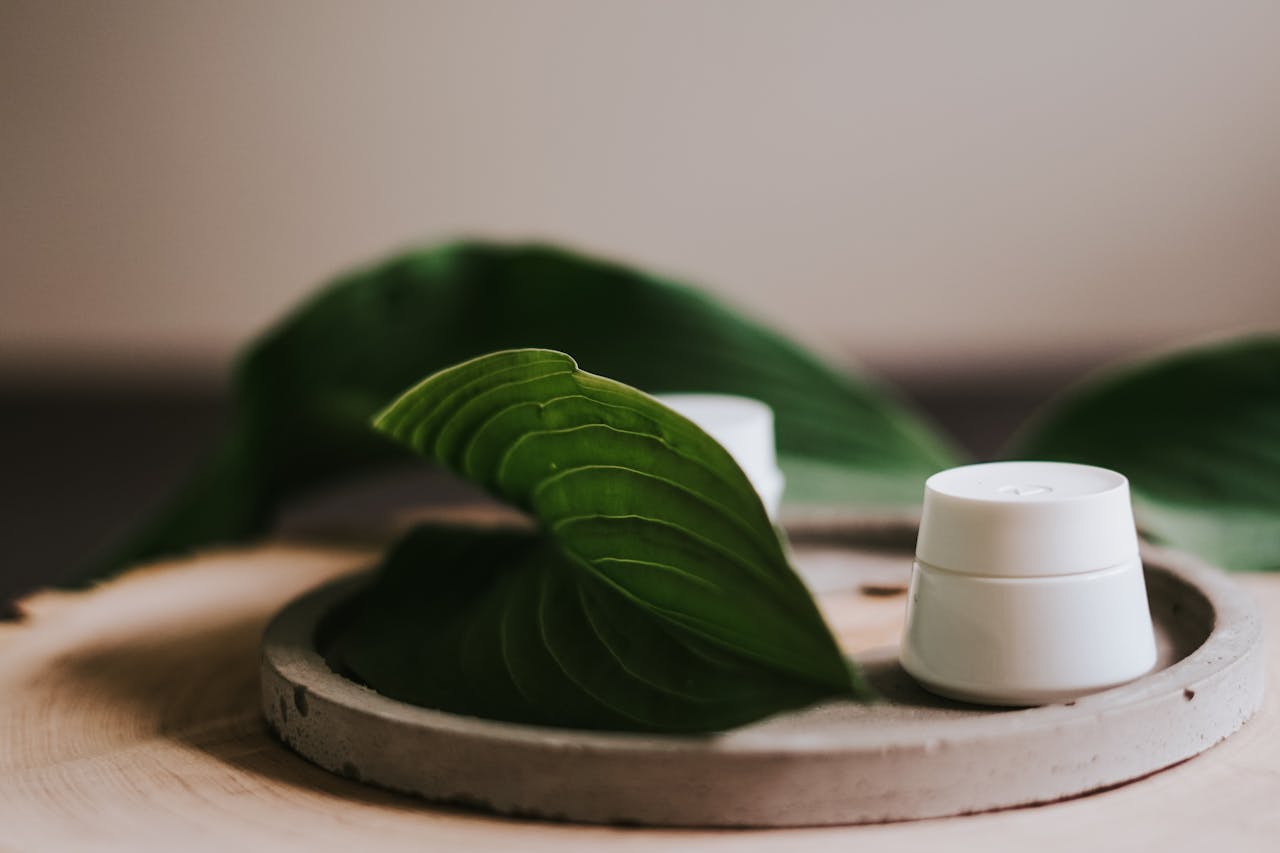 Close-up of cream containers with green leaves on wooden tray, promoting natural skincare.